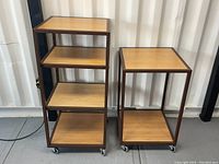 Front view of two wheeled shelving units, one with four shelves and the other with two. Shows wood-like shelves and brown steel frame construction.
