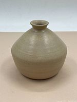 Front view of the beige rounded pottery vessel tapering to a narrow neck and lip, showing texture and wheel marks.