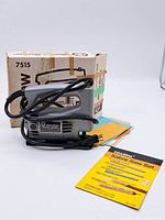 Gray Black & Decker 7515 Jig Saw with black power cord, original box and instruction booklets behind it on white surface.