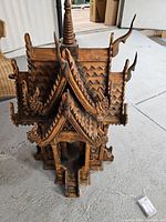 Top and slightly angled view of the carved wooden doll house showing detailed roof design and finials