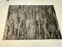 Full view of the black patchwork cowhide rug laid out flat, showing rectangular patchwork pattern and natural color variation.