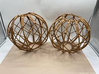 Pair of vintage wicker orbs shown side by side on a beige surface against a white background. Both have open lattice design with thicker wooden strips.