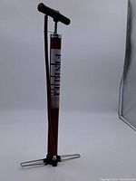 Full view of the red metal hand air pump with black T-handle and foldable foot stands.