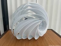 Close-up of the white spiral light shade showing the swirling strips that form a spherical shape with a hollow center, placed on a wooden surface.