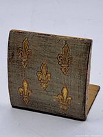 Front view of the desk-top paper holder showing five raised fleur-de-lis motifs on gilded metal surface.