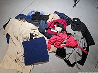 Photo of assorted vintage clothing items piled on floor showing various coats, dresses, and jackets in multiple colors.