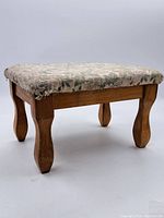 Full view of the small upholstered footstool showing wooden legs and floral top.