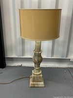 Front view of the vintage stone base table lamp with beige shade on gray floor.