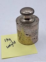 Metal vintage weight showing overall cylindrical shape with rounded top handle and visible tarnish and wear.