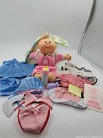 Main lot photo showing baby doll, multiple outfits, baby bottle, and sleeping bag.