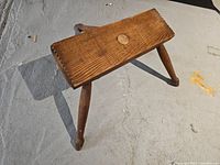 Side-angle view showing top and two legs of the wooden stool on concrete floor.