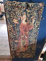 Full view of the tapestry showing the woman in a red dress holding a flower with detailed botanical background