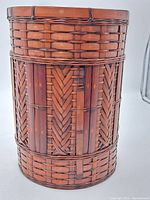 Front view of vintage woven wicker waste bin showing detailed vertical and herringbone weaving patterns and reinforced top rim.