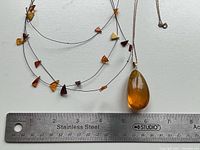 Amber drop pendant with gold loop beside ruler for size reference, also showing part of a multi-amber chip necklace.