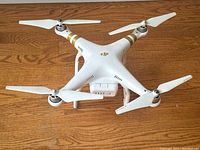 Top-down view of drone showing white body, gold arm stripes, four propellers