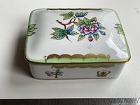 Closed view of rectangular porcelain trinket box with floral and butterfly designs and gold trim.