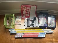 Overview of home improvement tools and supplies including pneumatic nailer, Philips fluorescent lights, magnetic mesh screen doors, garage sale signs, and metal hardware in a green bin.