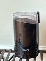 Front view of black Krups coffee grinder with clear lid, showing the brand name on the front.