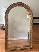 Full view of the arched gilt mirror showing the entire frame and reflective surface.