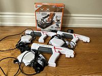 Three white Laser X laser tag guns, each with attached black straps, and the Hexbug VEX Robotics kit box sitting on the floor.