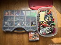 View of the lot with a transparent plastic storage box showing multiple compartments filled with assorted Lego pieces, a large translucent container filled with assorted Lego parts and base plates, and a boxed Star Wars Chewbacca Lego fighter set positioned in front of the containers.