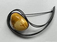 Top view of the brooch showing the large polished egg yolk amber stone set within a dark silver modernist curved wire frame.