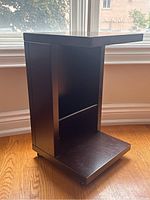 Front angled view of modern dark wood rolling side table showing open shelf design and surface wear.