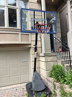 Side view of entire basketball net setup showing wheeled black base, black support pole, transparent backboard with blue and black trim and red hoop with net.