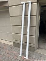 Two white vertical retractable screen door frames leaning against beige stone wall outside garage.