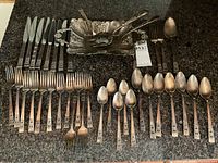 Full display of silver plated flatware set including knives, forks, spoons, serving utensils, and serving tray on granite countertop.