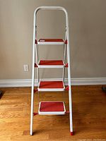 Front view of ErolTekNik 4-step folding step ladder showing four red slip-resistant steps and white frame.