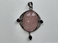 Front view of sterling silver pendant featuring a large oval rose quartz cabochon in the center with garnet stones and silver scrollwork around it.