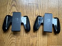 Two Nintendo Switch Joy-Con controller grips placed on wood floor, showing front views with Nintendo Switch logos visible.