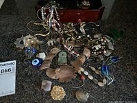 Overview of assorted vintage costume jewelry pieces on countertop including necklaces, brooches, and charms with wooden jewelry box in background.