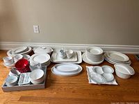 Photo showing white dinnerware collection with plates, bowls, ramekins, serving platters, and kitchen accessories arranged on floor.