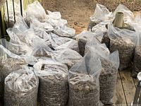 10 plastic bags filled with river rock and soil mixture arranged outdoors on paved surface.