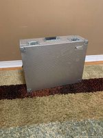 Side view of the textured silver aluminum case standing upright on carpet.