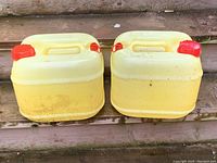 Top view showing two yellow chlorine jugs with red screw caps and integrated handles, placed side by side on wooden steps.