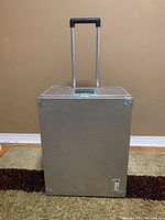 Front view of large aluminum case with pullout handle extended and wheels visible at bottom.