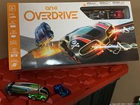 Main boxed Anki Overdrive game set with two extra vehicle pieces in front: green transport truck and blue sports car