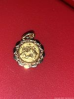 Close-up of antique gold baptism pendant showing the detailed central engraving and scalloped edges against a red background.