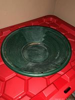 Full view of a green plastic gold pan showing wear marks and ridged sides for panning.