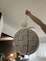 Unique white spherical hanging light fixture with black puzzle piece line pattern, shown being held to display size and shape.