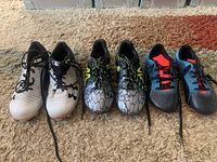 Three pairs of kids cleats displayed side by side on carpet.