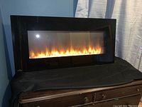 Front view of the black framed electric fireplace showing the lit flame effect behind a clear glass panel.