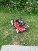 Front angle of the red Toro Recycler lawn mower on grass, showing the engine and handle, with visible wear on wheels and light surface rust.