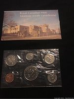 Plastic sealed pouch containing seven 1976 Canadian coins in uncirculated condition, visible denominations include penny, nickel, dime, quarter, half dollar, dollar, and a commemorative coin.