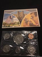 Photo showing six different Canadian coins from 1979 in sealed transparent plastic including 1 cent, 5, 10, 25, 50 cents, and $1 coin, alongside illustrated card featuring Canadian landmarks and mint-related artwork.