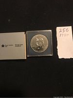 Overall view of the Royal Canadian Mint packaging, silver dollar coin in blue display case, and handwritten note with lot number and year