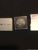 Photo showing the 1990 Canadian silver dollar in the original plastic case along with Royal Canadian Mint packaging and a handwritten note with year '1990'.